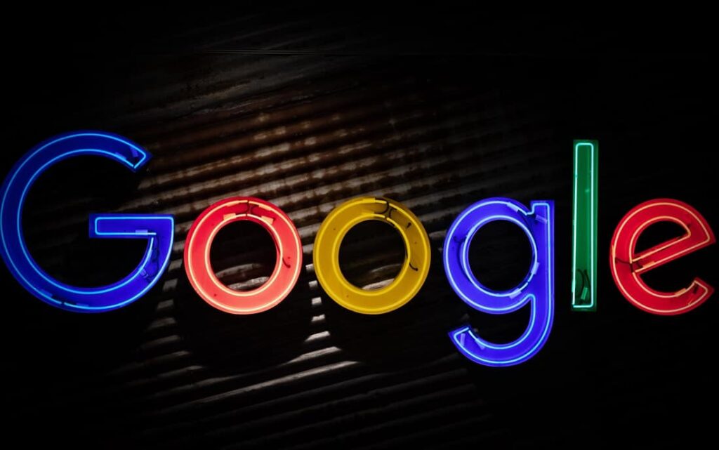 Enseigne néon colorée affichant le mot "Google" sur un fond sombre et texturé. Les lettres sont éclairées en bleu, rouge, jaune et vert, créant un contraste visuel saisissant.