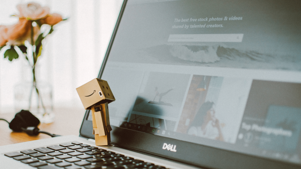 Un personnage en carton avec un logo Amazon regardant un écran d'ordinateur portable, illustrant l'optimisation des campagnes publicitaires sur Amazon Ads.